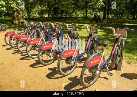 London, England - July 2018: Rental bicycles in their docking stations at the entrance to a park in central London. Stock Photo