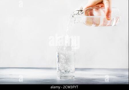 Clear water is poured from glass bottle into glass, gray background, selective focus Stock Photo