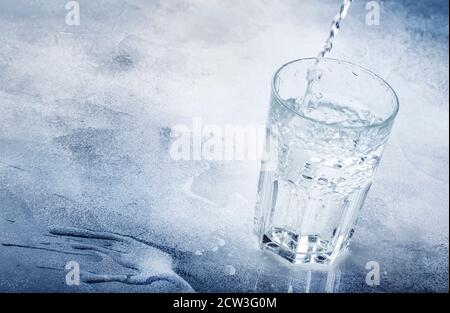 Clear water is poured from glass bottle into glass, gray background, selective focus Stock Photo