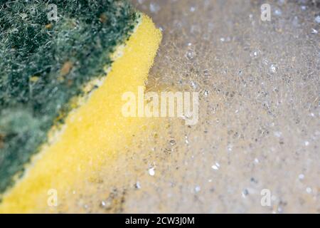 A sponge surrounded by washing up bubbles from washing up liquid using selective focus Stock Photo