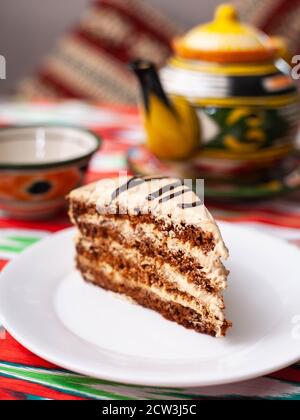 dessert chocolate cake with beige cream in oriental style on a rooftop with a teapot and a cup for tea. Stock Photo