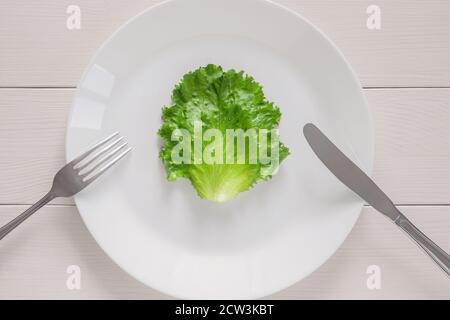 leaf lettuce on white plate with fork and knife, top view on wooden table Stock Photo