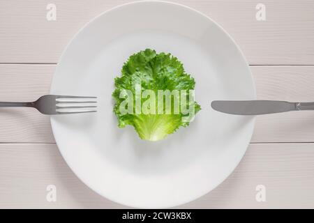 leaf lettuce on white plate with fork and knife, mono diet for weight loss Stock Photo