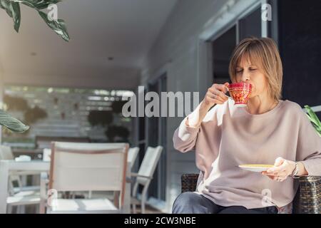 Middle-aged woman drinking coffee or tea enjoying on the balcony. Stock Photo