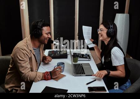 Portait of two cheerful radio hosts, young man and woman laughing while discussing various topics, moderating a live show in studio Stock Photo