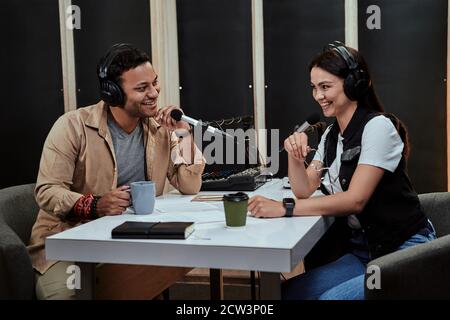 Portait of two happy radio hosts, man and woman smiling while talking with each other, moderating a live show in studio Stock Photo