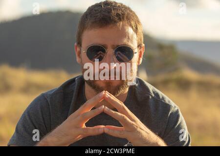 A young man, wearing glasses, concentrating on himself, meditates in a relaxed way, while enjoying the afternoon sun on a promenade in northern Spain. Stock Photo