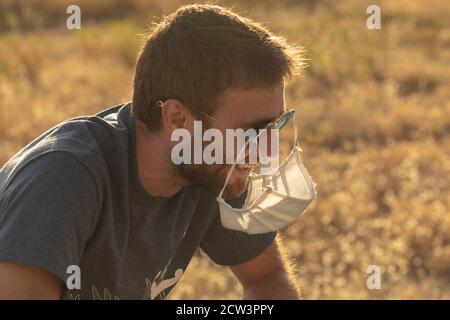 A young man laughs foolishly, as he hangs his protective face mask from his sunglasses. Stock Photo