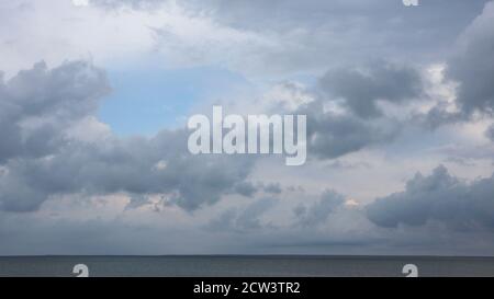 Grey high layered grey epic clouds on blue sky above thin sea water line. Heaven cloudscape air view Stock Photo