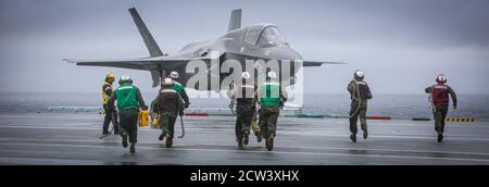 Marines with Marine Fighter Attack Squadron 211 move through the rain on the flight deck of HMS Queen Elizabeth at sea on 23 September, 2020. The Marines of the “Wake Island Avengers” are capable of fixing and flying 5th generation aircraft during adverse weather conditions. . Consistently operating and evaluating our aircrews and aircraft allows us to remain an integral part of the Fleet Marine Force and train to respond to any crisis, anywhere. Stock Photo