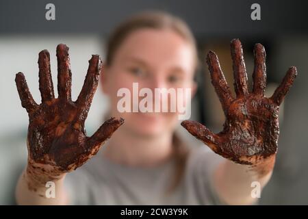 Cheerful girl showing her hands covered with chocolate after making candies, shallow focus Stock Photo