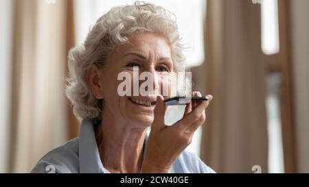 Pleasant mature female calling grandchild using voice dialing Stock Photo