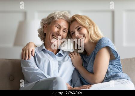 Two females of different generations embracing on couch at home Stock Photo