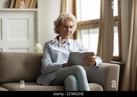 Peaceful pleasant senior woman using digital tablet pc indoors Stock Photo