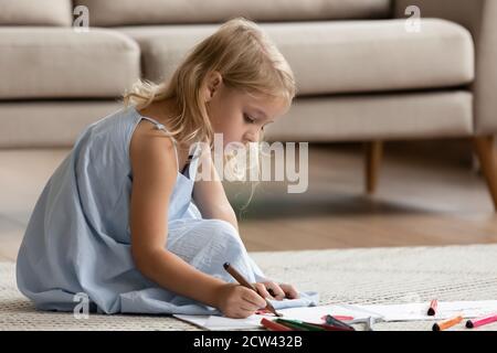 Inspired preschool girl sitting on warm floor drawing imaginary world Stock Photo