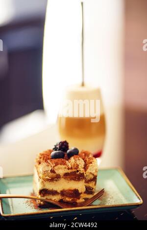 Cake decorated with fresh berries in a plate on the table in a cafe. Tiramisu cakes and cappuccino on table Stock Photo