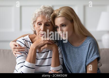 Sad grownup daughter sitting on sofa hugging desperate elderly mother Stock Photo