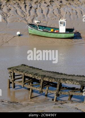 Pea green fishing boat moored on the muddy banks of the River Axe near Weston super Mare in Somerset UK Stock Photo