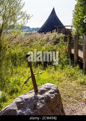 King Arthur's sword in the stone before a replica neolithic thatched crannog built over Llangors Lake in the Brecon Beacons of South Wales UK Stock Photo