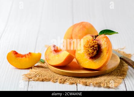Fresh sweet sliced peach with green leaf on wood plate and white wood  background. Peach fruits Stock Photo