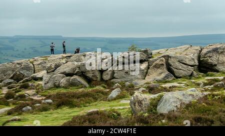 Three Asian lads enjoying the outdoors taking selfies & photos of each other - one doing a one-armed press up at the top of the Cow and Calf Rocks, UK Stock Photo