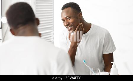 African American Man Touching Face After Shaving Standing In Bathroom Stock Photo