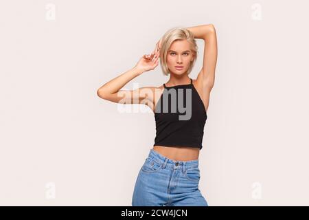 Freestyle. Young blonde woman in jeans and top standing isolated on white hands up posing to camera confident Stock Photo