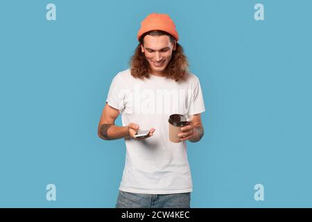 Young adult guy using smartphone, holding cup with beverage in hand Stock Photo