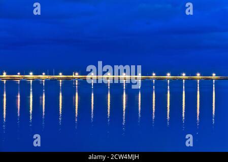 Beautiful harbor's lanterns lighting in the evening. Reflection of light in the water. East pier of Dun Laoghaire harbor during the blue hour, Dublin Stock Photo