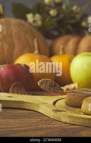 Chocolate cookies and autumn harvest on wooden table. Ripe pumpkins, apples and persimmons on background. Spoon with spices or chocolate chips. The concept of Christmas, Thanksgiving and Halloween.