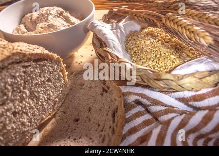 Wicker basket with wheat and some ears of wheat, homemade wholemeal bread and a cup of sourdough Stock Photo