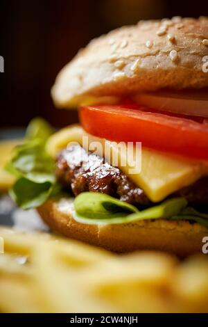 cheeseburger surrounded by french fries on a black table Stock Photo