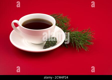 A Cup of coffee on a white saucer, pine branches and cones on a red background. Stock Photo