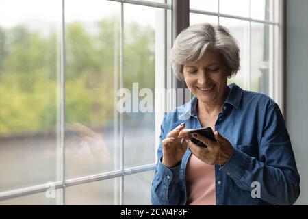Happy elderly woman have fun using smartphone gadget Stock Photo