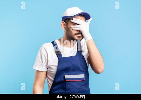 Curious, suspicious handyman in overalls and hygiene gloves looking through fingers, spying secret. Profession of service industry, courier delivery, Stock Photo
