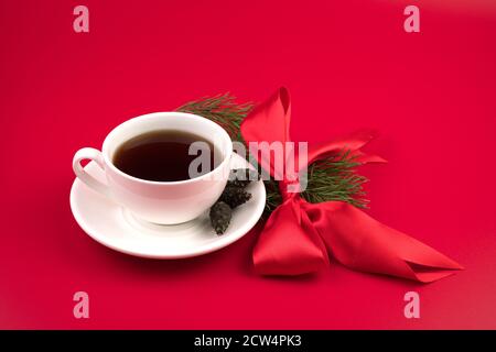 Coffee Cup on a white saucer with a red bow, pine branches and cones on a red background. Stock Photo