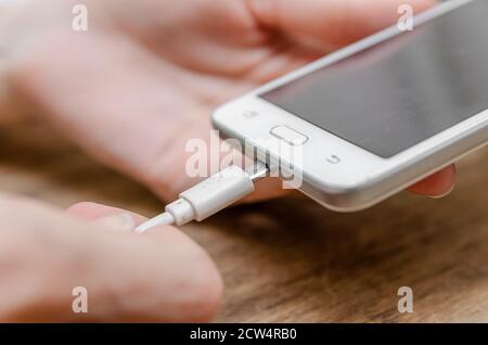 Female hand connecting a white lightning charging cable to a mobile phone - USB data cable to a modern gadget. Close up Stock Photo