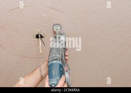 A man holds a power drill in his hands. Make a hole in the ceiling. Repair work in the apartment. Restoration indoors. Stock Photo