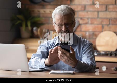 Smiling old man use smartphone work on laptop Stock Photo