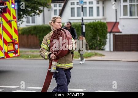 Woman Firefighter rolls out the hose with London Fire Brigade attending a house fire in a residential street, South London, England, United Kingdom