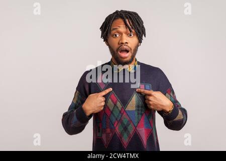 Extremely surprised shocked african man with dreadlocks pointing fingers at himself with widely open eyes and mouth, wondered with choice. Indoor stud Stock Photo