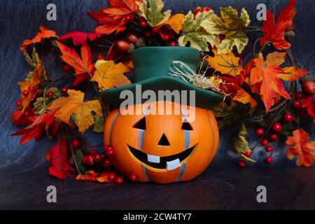 Artificial Orange Halloween Pumpkin with Green Hat. Artificial Autumn Leaves. Halloween and Fall Vibes. Stock Photo