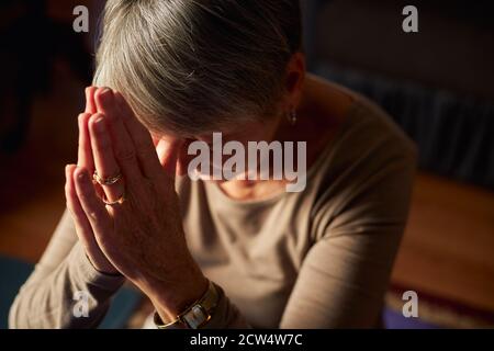 Close Up Of Senior Woman At Home Praying Or Meditating With Hands Together Stock Photo