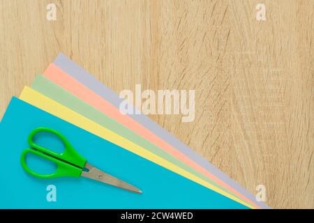 Top view of multicolored paper and scisors on wooden table. Top view.  Arrangement for creative work or craft. Stock Photo