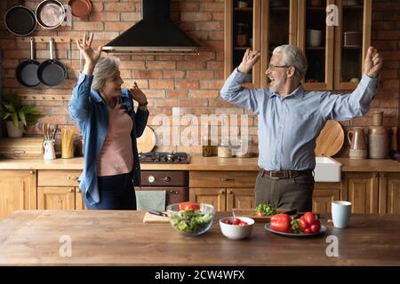 Excited healthy senior couple dance cooking together Stock Photo