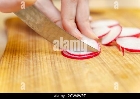 Female hands cut radish into circles on a wooden board closeup Stock Photo