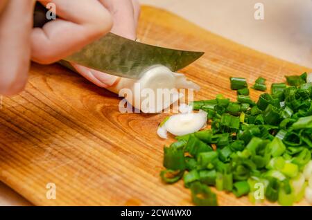 Female hands chopping green onion with a knife on a wooden board closeup. healthy eating, cooking, vegetarian food Stock Photo