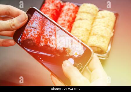 A girl photographs red and white sushi on the phone from different angles. Photo close up. photo with flare Stock Photo