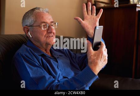 Smiling Senior Man At Home Waving As He Makes Video Call To Family On Mobile Phone Stock Photo
