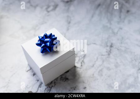 Christmas gift box or present with ribbon end bow isolated on grey marble background. Festive blue gift bow.Copy space for greeting text. Stock Photo